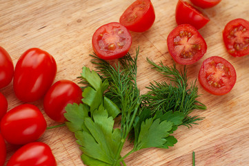 Ripe cherry tomatoes with parsley and dill in a wooden cutting board, top view