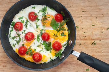 Fried eggs with cherry tomatoes, parsley and dill in a pan