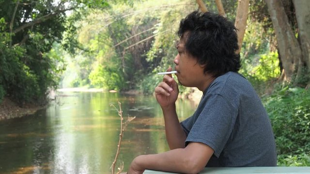 Asian handsome man is sitting and smoking in the forest.