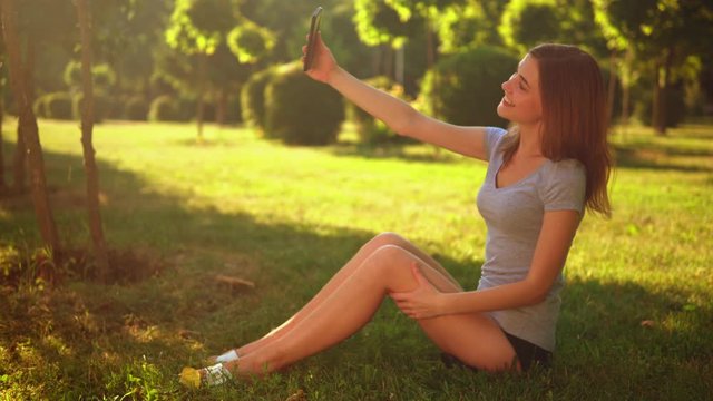 happy smiling young woman in casual t-shirt and denim shorts holding smartphone holding smart phone sharing video in social media on the background beautiful summer garden
