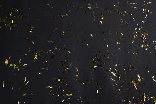 Festive party or carnival decoration golden bright confetti and coiled streamers falling against black background.
