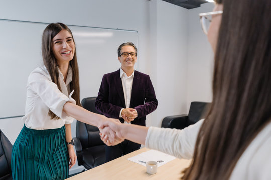 Candid smile and friendly handshake between HR manager and job applicant with smiling senior recruiter in the background