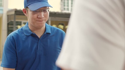 Young postal delivery courier man holding parcel boxes for sending to customer, Asian men signing and pay via qr code on mobile phone for receive delivered parcels outdoors.