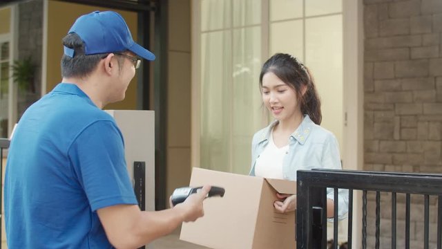 Young postal delivery courier man holding parcel boxes for sending to customer, Asian women signing and pay via qr code on mobile phone for receive delivered parcels outdoors.