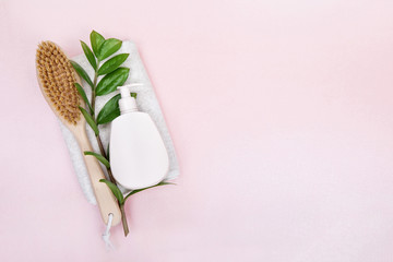  Brush for dry massage , body cream and  green leaves on linen towel over pink background. flat lay top view