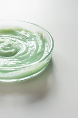 Close-up hair shampoo texture in glass petri dish with selective focus. Cosmetic body and hair care product on white background, vertical