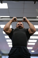 Naklejka premium chin up on bar of young strong caucasian man with beard in bright sport gym during hard workout
