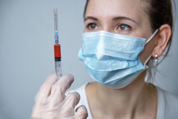 A nurse in a protective mask and gloves holds a syringe with a vaccine.