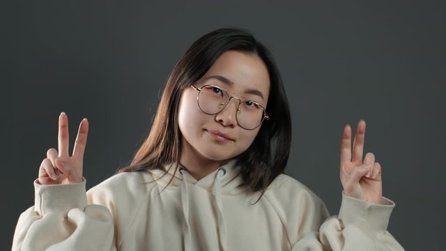 Pretty asian girl showing with hands and two fingers like quotes gesture, bend fingers isolated over grey background. Very funny, irony and sarcasm concept.