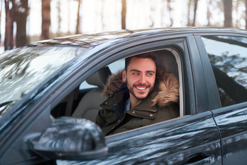 Young attractive Caucasian man sits at the wheel of his car sunny winter day.