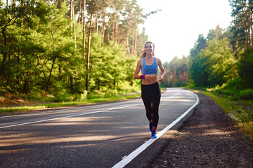 Beautiful caucasian young girl athlete runs sunny summer day on  asphalt road in the forest.