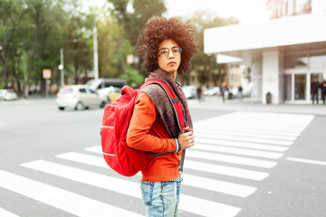 A young African American man with a red backpack crosses the road