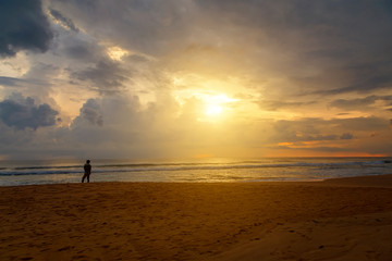Man silhouette stand alone on stony beach and watching romantic colorful sunrise.