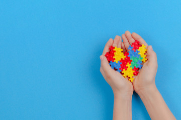 Kid hand holding colorful heart on light blue background. World autism awareness day concept