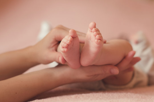 Mother holding baby feet in bed over pink background close up. Motherhood. Maternity.