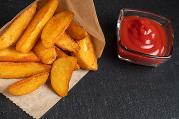 Rustic potato with ketchup on slate utensils, black stone.