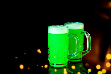 Mugs of green beer for celebrating St. Patrick's Day on the black background. Art design, bokeh. Celebrating irish holiday Saint Patrick's Day.