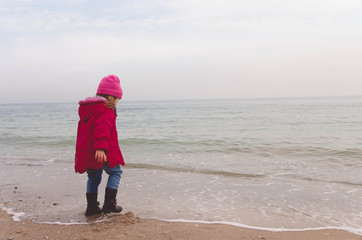 little girl in a red jacket plays with the waves on the beach