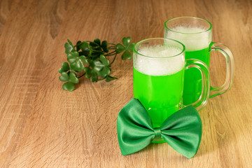 Symbols of celebrating Saint Patrick Day. Green bow tie, beer and leaves of shamrock on the wooden background. Traditional irish festival.