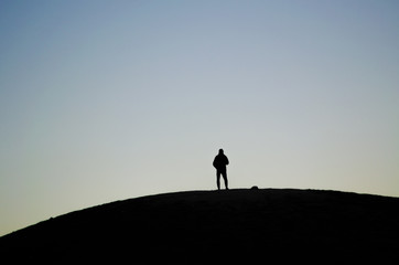 Silhouette of a person placed in the middle of a hill during a sunrise