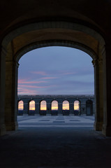 Dark tunnel leading to a large courtyard lined with arches in the middle of a colorful sunset