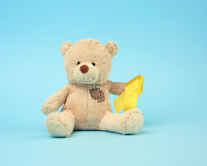 Cute brown teddy bear with a patch holds a silk yellow ribbon in the shape of a loop