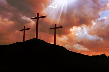 A dramatic red stormy sky above three crucifix silhouettes on a dark hill, with a break in the cloud and rays of light shining down