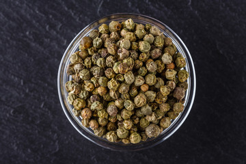 green peppercorns on dark slate stone background