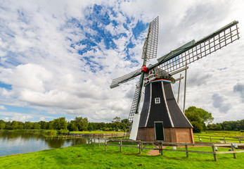 Wide angle view of a dutch landscape, with meadows, canals and an ancient black and white windmill in the foreground © Roberto