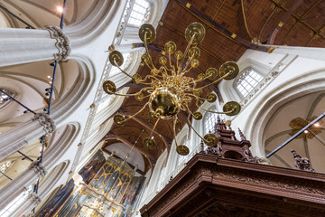 Wide angle view from below of the vault of a dutch cathedral, with a golden chandelier and a row of pointed arches