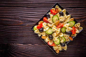 Delicious pasta salad with tomato cucumber and olives on wooden rustic background