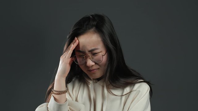 Young korean asian woman with long hair having headache, studio portrait. Girl putting hands on head, isolated on grey background. Concept of problems and headache.