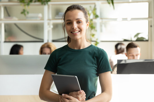 Portrait of smiling millennial Caucasian girl graphic designer pose holding modern tablet, profile picture of happy young female employee worker stand with pad in coworking office, internship concept