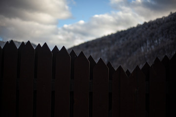 Wooden fence at the house in the mountains. Toothed fence on the background of a hillside. The fence around the building made of wood.