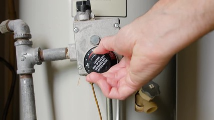Plumber adjusting thermostat temperature dial on natural gas hot water heater. Residential boiler tank controls for heating household water.