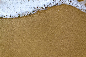 wave with foam on a sandy beach, copy space