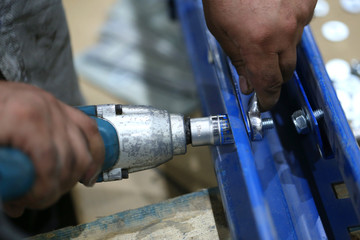 One warehouse worker in with power tool tightening screw during rack arrangement erection work