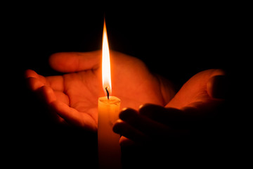 Hands holding a burning candle in dark. The concept of hope and warmth. Spirituality and prayer....