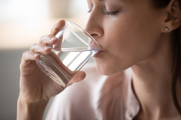 Side view head shot close up young woman drinking pure still water in morning. Healthy thirsty lady...