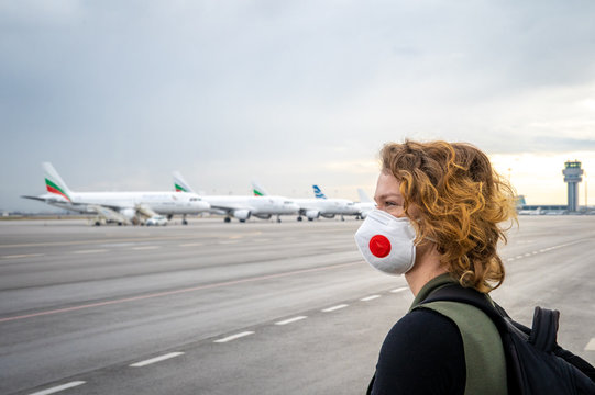 Woman with a mask on her mouth protects against the virus. Sadly looks at the aircraft parked at the airport. Canceled flights due to coronavirus