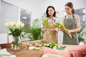 Waist up portrait of two female florists arranging flower compositions and bouquets with Spring...
