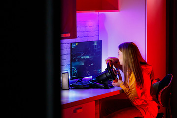 girl gamer playing racing on a computer. She uses a steering wheel. emotional play