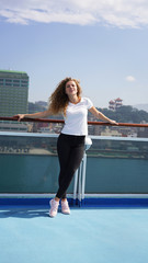 Happy beautiful girl on summer vacation on a cruise liner dreamily looks away and smiles against the backdrop of the port Asian city, a walk on the deck of the ship in sunny weather.