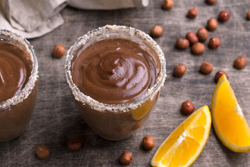 Chocolate mousse with cream, hazelnuts and orange in glasses on old dark wooden table.