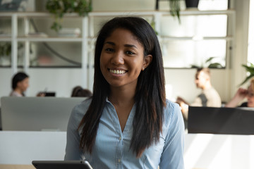 Profile picture of smiling African American millennial female employee posing in coworking space holding tablet, headshot portrait of happy biracial woman worker stand in office, internship concept - Powered by Adobe