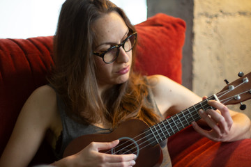 Young beautiful woman playing ukelele in grey dress indoors