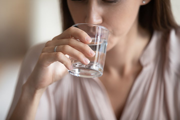 Close up cropped image young woman holding glass, drinking fresh still pure water. Happy lady...