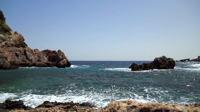 Small wave crashes on the rocks in slow motion.