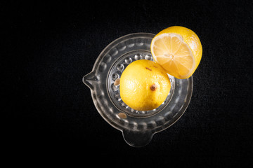 Lemon cut in half, on a glass lemon squeezer. Black background