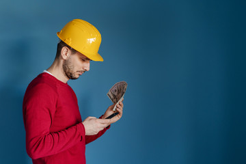 Portrait of young caucasian man wear red sweater in front of blue background with protective helmet...